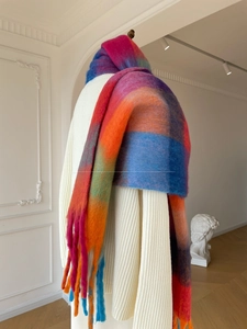 Close-up of thick multi-color plaid shawl with fringe tassels on white knitwear