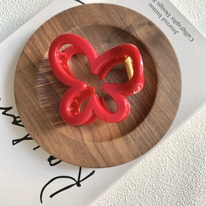 Close-up of a red butterfly hair claw clip on a wooden tray with a book background