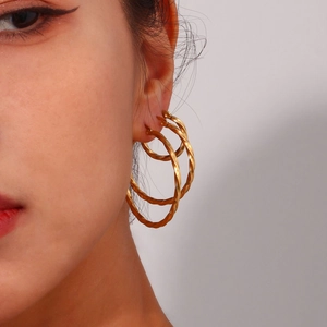 Close-up of golden twisted hoop earrings with textured finish worn on a model