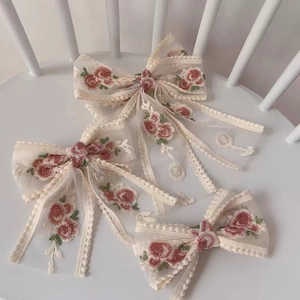 Detailed view of elegant white lace hair bows with red rose embroidery accents.