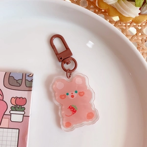 Close-up of pink bear acrylic keychain with brown metal lobster clasp on a white plate