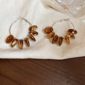 Detail of silver hoops with amber resin marble beads on a beige linen background