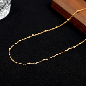 Minimalist golden titanium steel beaded chain necklace on textured black background