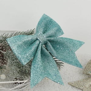 Sparkling turquoise glitter Christmas bow ornament hanging on a snowy pine tree branch