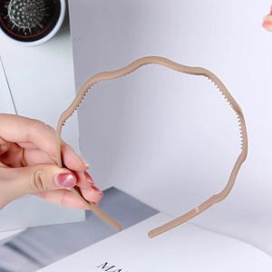 Detail of khaki wavy plastic headband with anti-slip inner teeth held by hand