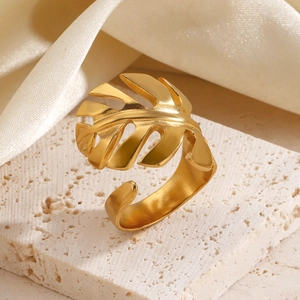 Vergoldeter Edelstahlring mit Monstera-Blatt Design auf Stein und Seide Hintergrund