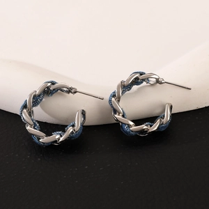 Detail of silver chain and blue denim fabric woven twist design on C-shaped hoop earrings