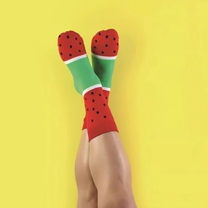 Vibrant watermelon patterned mid-calf socks shown in a playful cross-legged pose on yellow