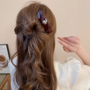 Detail view of dark red acrylic hair clip with gold logo on half-up hairstyle