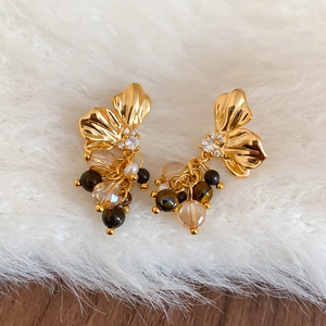 Detail of golden butterfly earrings with crystal tassels and brown beads on plush background