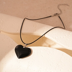Vintage black heart pendant necklace with leather cord and silver clasp on stone surface