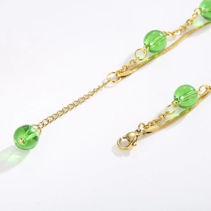 Close-up of golden stainless steel chain with green pearls and lobster clasp detail