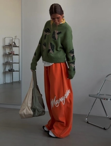 Detail of green knit sweater with mushroom pattern and orange wide-leg casual pants