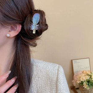 Détail d'une pince à cheveux plume colorée avec dégradé bleu-violet et bords métalliques