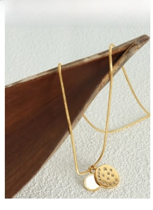 Detail of gold snake chain with zircon oval pendant and Good Luck round charm