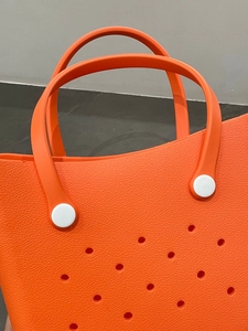 Close-up of orange EVA beach bag showing hole patterns and white rivet handle attachment