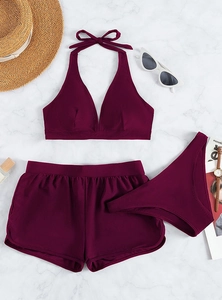 Flat lay of burgundy three-piece halter swimwear with bikini set and shorts on marble