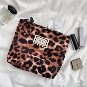 Dettaglio trousse leopardata con cerniera e toppa Pleasant Time su tessuto bianco