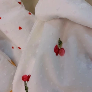 Detail of white dot fabric featuring delicate red cherry and heart embroidery