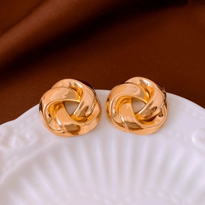 Close-up of gold love knot stud earrings on a textured tray with dark silk background