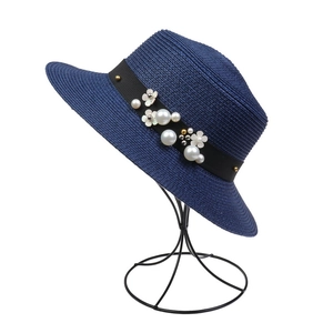 Detail of dark blue straw hat featuring pearl embellishments and white floral accents