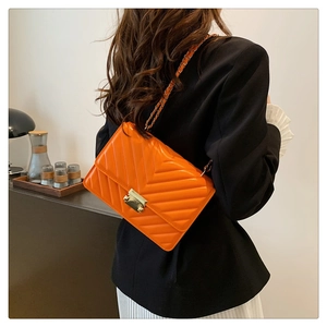 Detail of bright orange V-quilted shoulder bag with gold chain strap and metal buckle