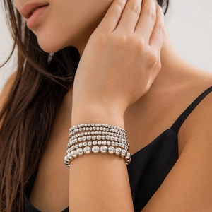 Close-up of stacked silver metal bead bracelets with heart charms on model wrist