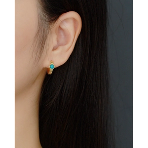 Detailed close-up of a gold huggie hoop earring with a turquoise stone on a female model