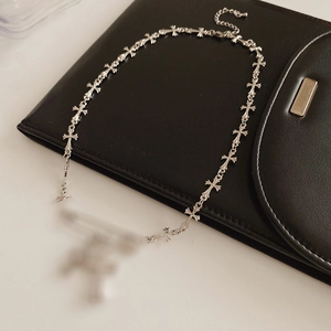 Detail shot of silver safety pin and zircon cross link necklace on black leather