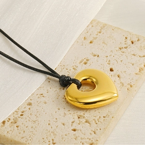 Close-up of polished gold heart pendant with a black cord on a minimalist stone base