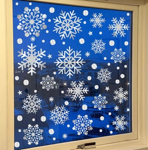 Close-up of silver snowflake static window decals on glass with winter night background