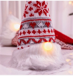 Close-up of a glowing Christmas gnome with red knitted snowflake hat and white faux fur beard