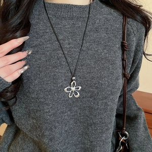 Detail of silver hollow flower pendant on a black cord necklace worn with a grey sweater