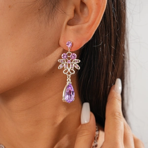 Detail of silver drop earrings with purple zircon floral clusters worn on ear