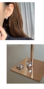 Close-up detail of silver smiley face hoop earrings on model and display stand