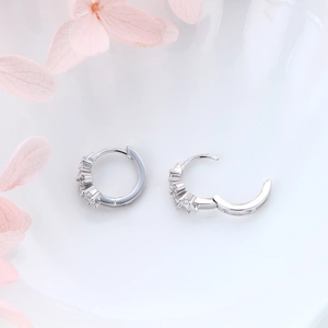 Close-up of small silver huggie hoop earrings with cubic zirconia on white background