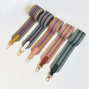 Detail of five woven wide bag straps with colorful geometric patterns and gold metal buckles