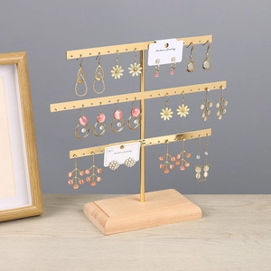 Three-tier gold metal earring stand with wooden base displaying various jewelry items