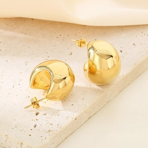 Gros plan de boucles d'oreilles créoles C en acier doré 18K sur un support en pierre