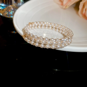 Detail view of triple-layer pearl bracelet with rhinestone rings on white porcelain
