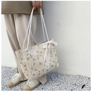 Close-up of woven straw tote bag featuring green leaf embroidery and lace bow detail