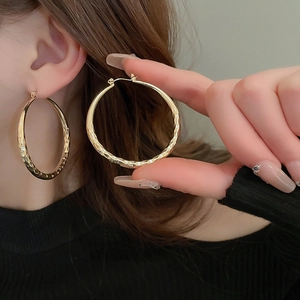 Macro shot of large gold geometric hoop earrings with textured diamond-cut surface pattern