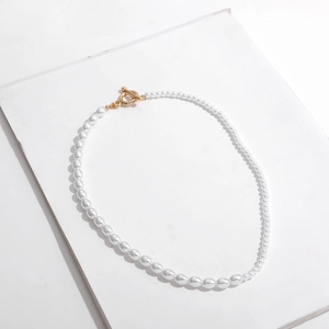 Detailed view of white pearls with a decorative gold OT clasp toggle on plain background