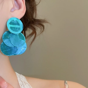 Close-up of a model wearing tiered teal circular resin tassel earrings for beach vacations