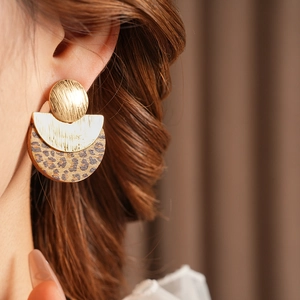 Detail of round leopard print and gold metal earrings worn by a model in soft lighting