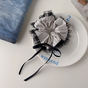 Detailed close-up of striped lace scrunchie with silk bow and pearl on ceramic tray