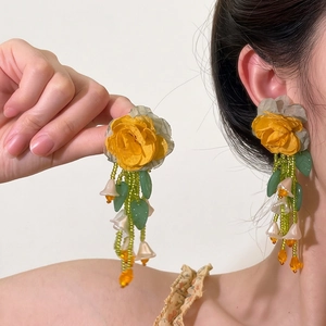 Detailed view of yellow rose flower earrings with green beaded tassels and lilies