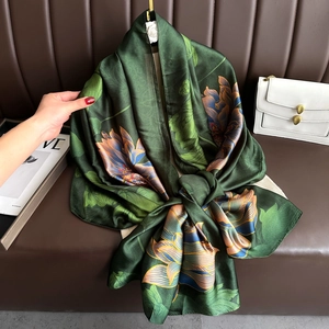 Detailed view of dark green silk scarf with large lotus print and glossy texture