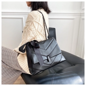 Detail of black quilted shoulder bag with large satin bow and chain strap on a model