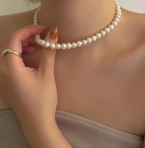 Detail of 10mm white pearl necklace on neck with minimalist silver ring on finger
